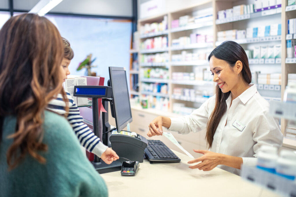Smiling pharmacist reading prescription while woman with her son standing at counter in drugstore.